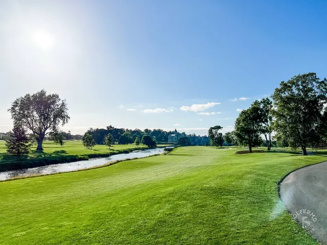 A golfer hitting a shot at Adare Manor, with the manor and the trees ahead.