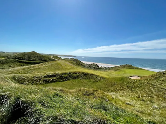A green and flagstick on the Cashen Course, with a bunker in front and the ocean behind the hole.