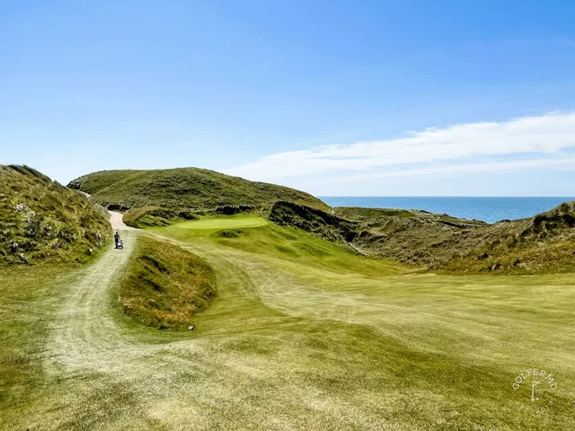 A golfer hitting a shot on the Cashen Course, with the fairway and the ocean ahead.
