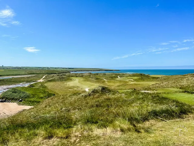 A green and flagstick on the Cashen Course above the water, with the ocean filling the background.
