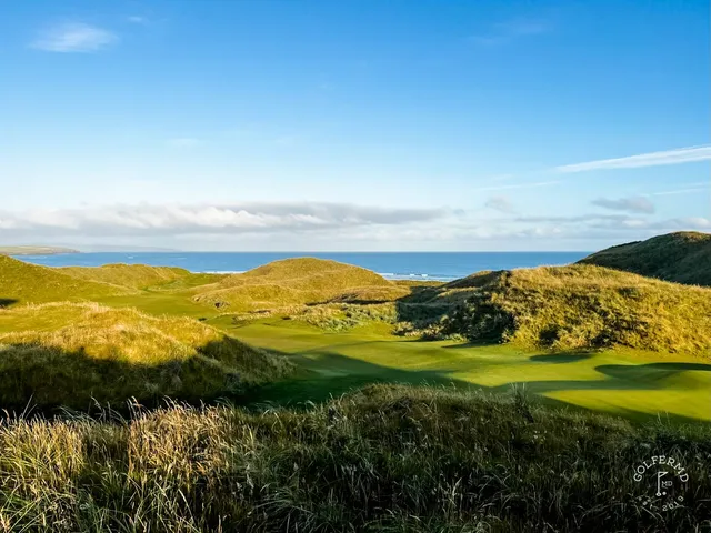A green and flagstick on the Old Course, with a bunker in front and the ocean behind the hole.