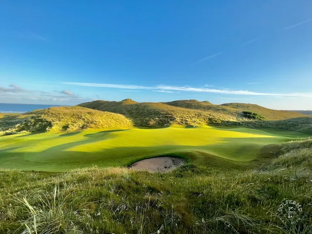 A golfer hitting a shot on the Old Course, with the fairway and the ocean ahead.