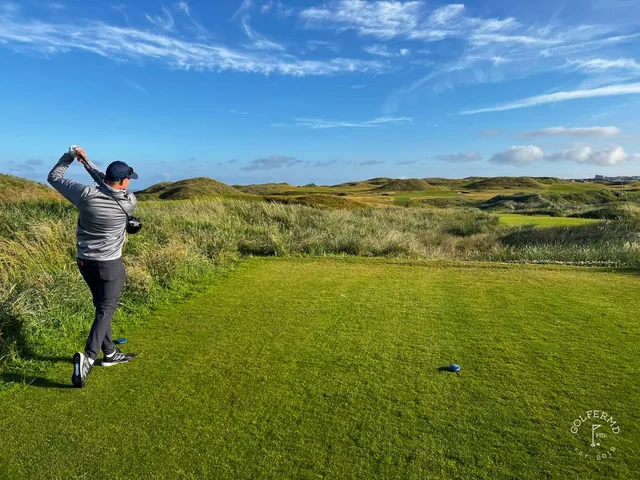 A green and flagstick on the Old Course above the ocean, with a bunker short of the green.