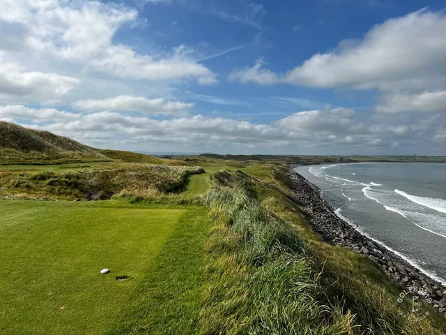 A green and flagstick on the Old Course, seen from a rise, with the ocean behind the hole.