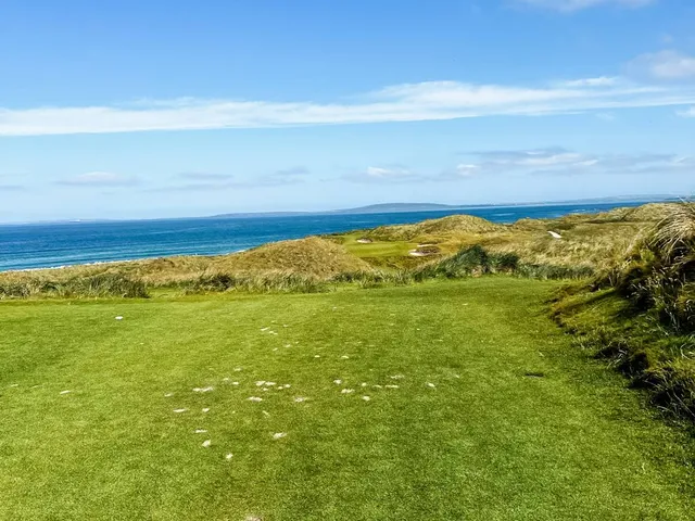 A close view of a flagstick on the Old Course, with the Atlantic behind the green.