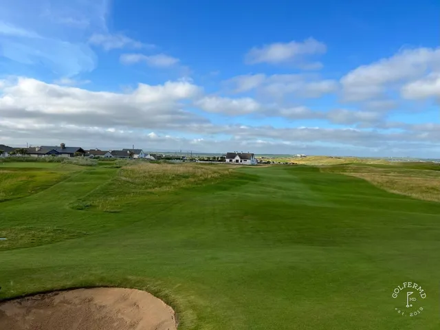 A green and flagstick on the Old Course, with sand in front and the ocean on the horizon.