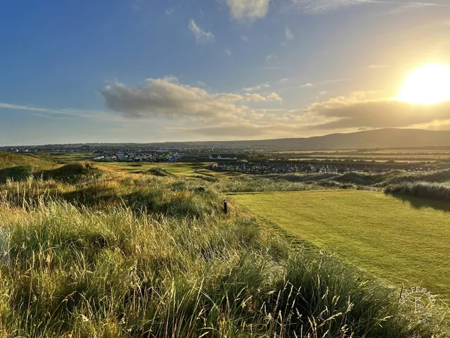 A close view of a flagstick on the Old Course, framed by the dunes and the Atlantic.