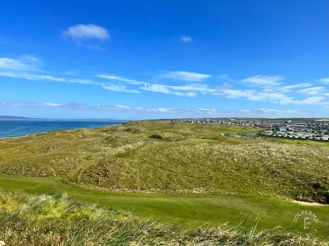 A close view of a flagstick on the Old Course, with the Atlantic behind the green.