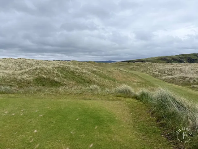 A golfer putting on a green on the Glashedy Links, with the ocean beyond the hole.