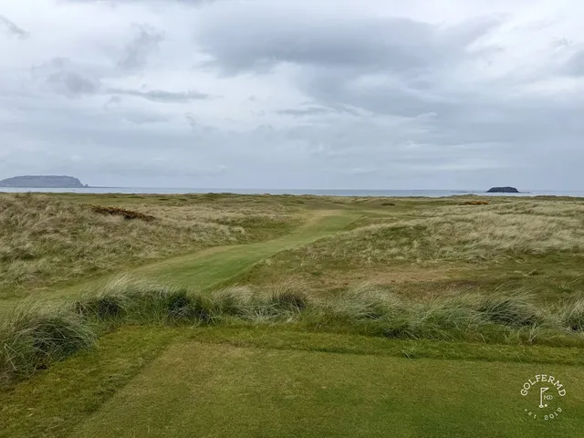 A close view of a flagstick on the Glashedy Links, with dunes and the ocean behind the green.