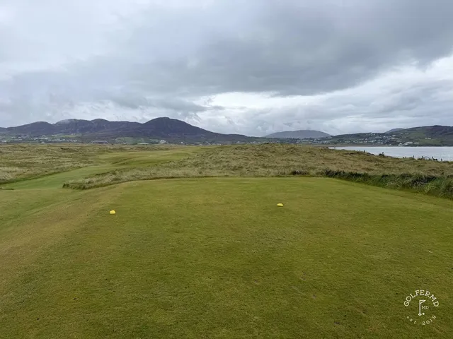 A golfer putting on a green on the Old Links, with the ocean beyond the hole.