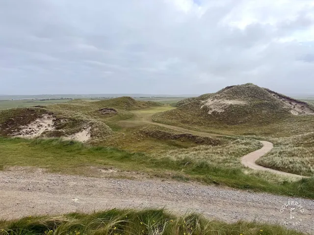 A green and flagstick at Carne, with a bunker in front and the ocean behind the hole.