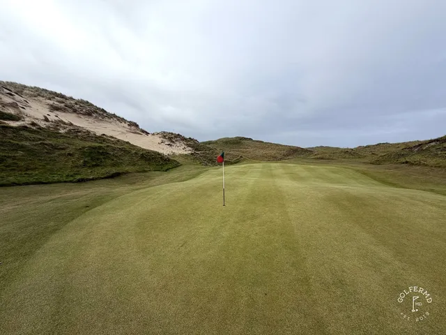 A golfer hitting a shot at Carne, with the fairway and the ocean ahead.