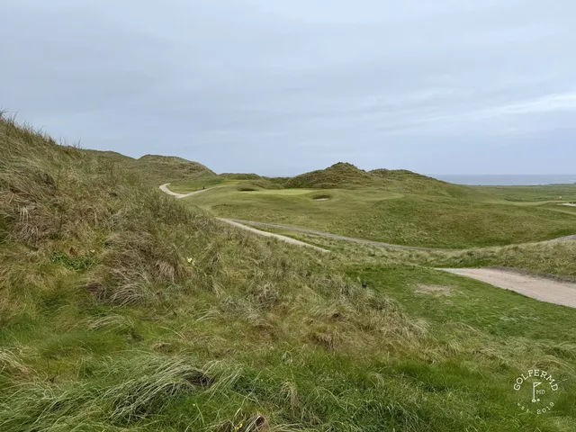 A green and flagstick at Carne above the water, with a bunker short of the green.