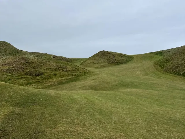 A golfer putting on a green at Carne, with the ocean beyond the hole.