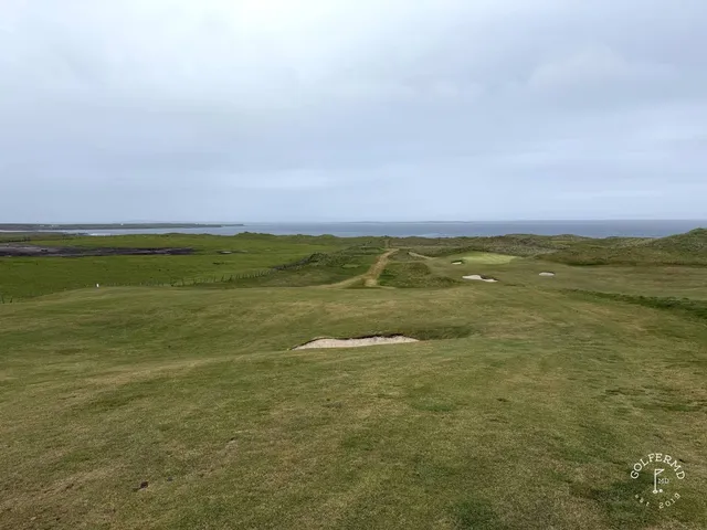 A fairway and green at Carne, with a bunker in the foreground and the ocean beyond.