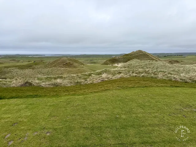 A green and flagstick at Carne, seen from a rise, with the Atlantic behind the hole.