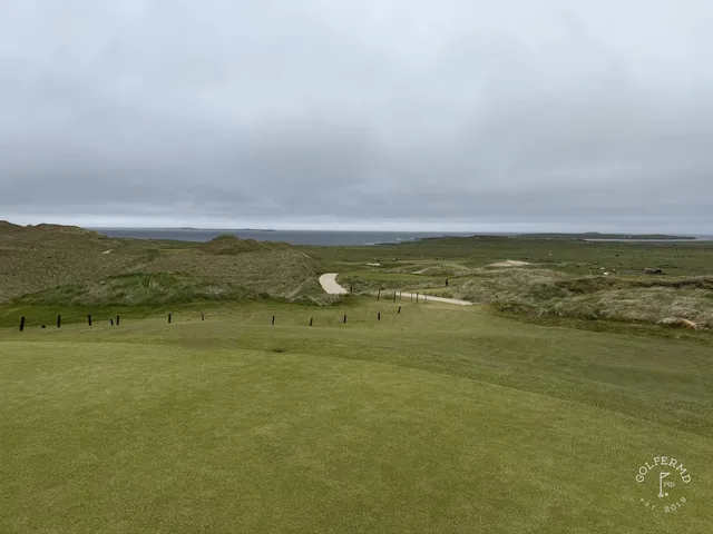 A close view of a flagstick at Carne, with the ocean behind the green.