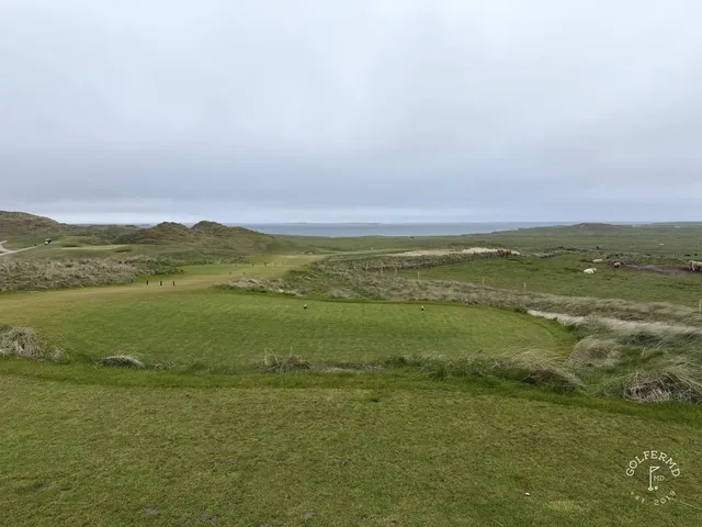 A green and flagstick at Carne, with a deep bunker in front and the ocean beyond.