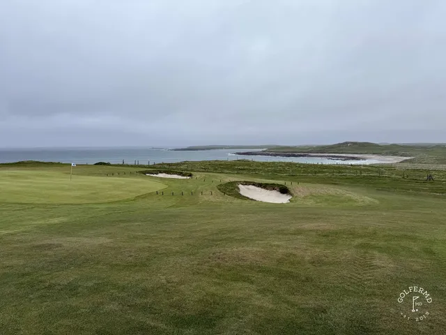 A golfer hitting a shot from the dunes at Carne, with the water ahead.