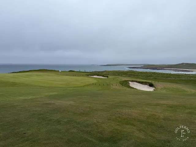 A green and flagstick at Carne, with sand in front and the bay on the horizon.