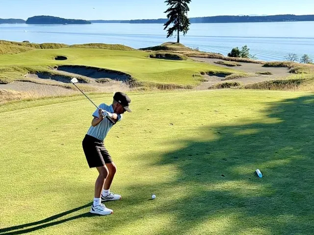 A golfer hitting a shot from the sandy rough at Chambers Bay, with the sound ahead.