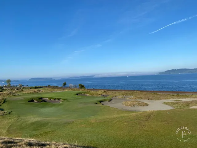 A close view of a flagstick at Chambers Bay, with the sound and the mountains beyond.