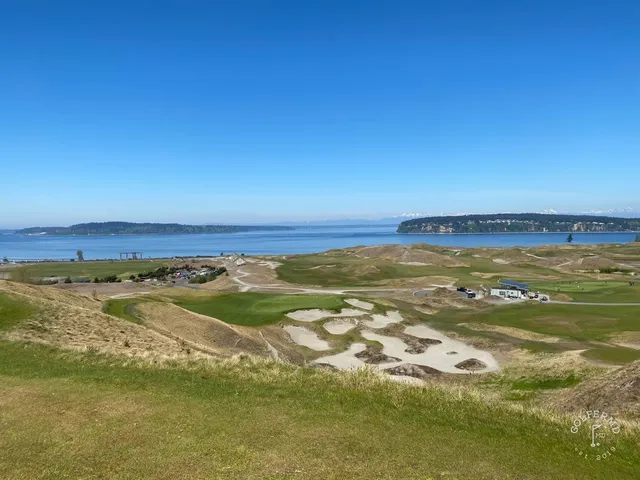 A green and flagstick at Chambers Bay, with sand short of the green and the water beyond.