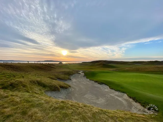 A green and flagstick at Chambers Bay, with a bunker in front and the water behind the hole.
