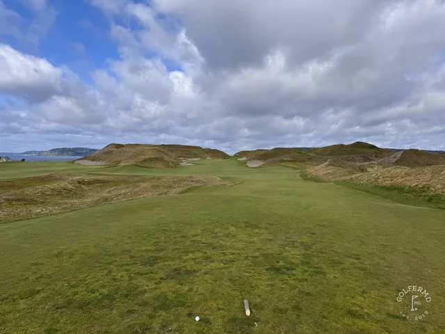 A golfer hitting a shot at Chambers Bay, with the fairway stretching toward the water.