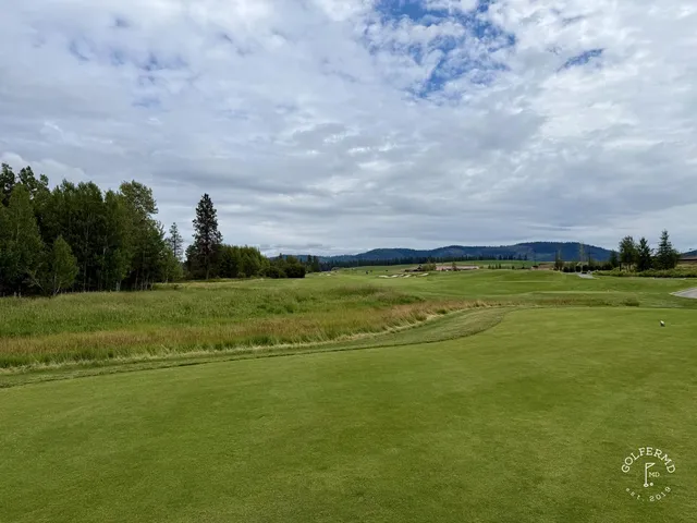 A close view of a flagstick at Circling Raven, with the green and trees behind it.