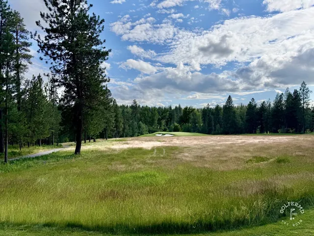 A fairway at Circling Raven curving through the trees toward a green.