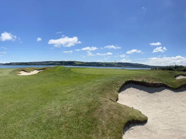 A green and flagstick at Cork Golf Club, with a bunker in front and the water behind the hole.