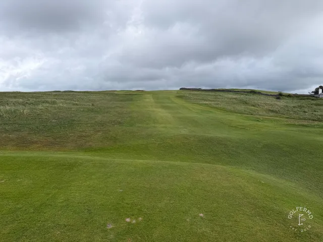 A golfer hitting a shot at Rosses Point, with the ocean and Benbulbin ahead.