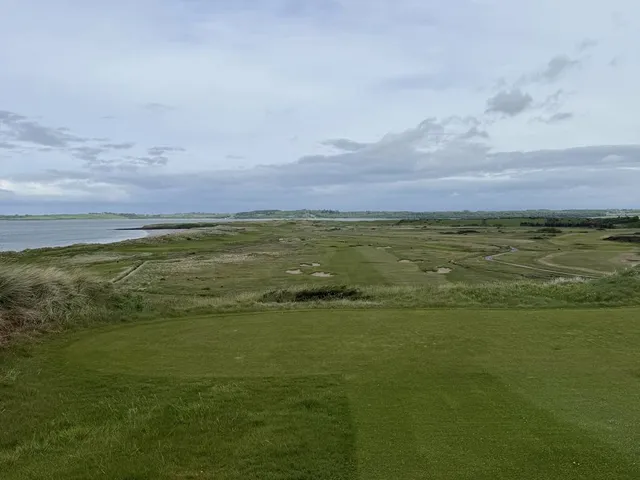 A fairway and green at County Sligo, with a bunker in the foreground and the bay beyond.