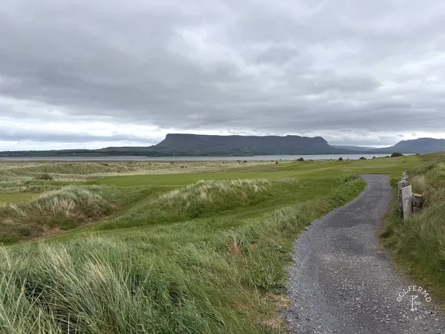 A green and flagstick at County Sligo, with sand in front and the mountain on the horizon.