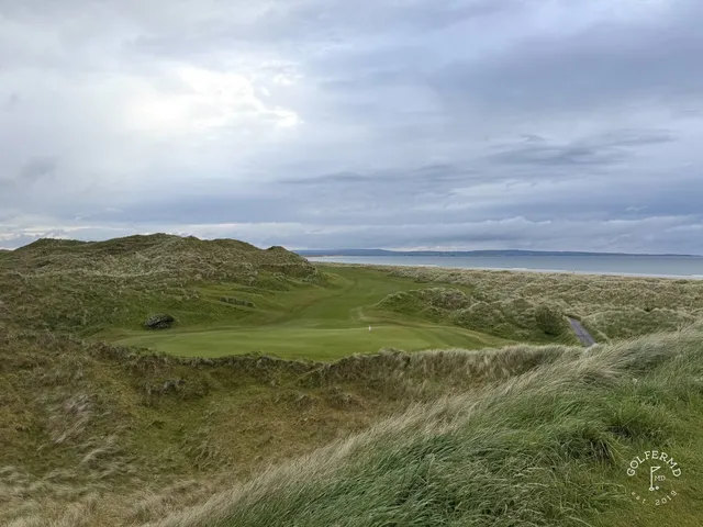 A close view of a flagstick at Enniscrone, with the ocean behind the green.