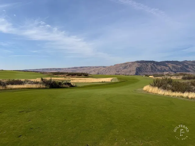 A tee shot at Gamble Sands, the fairway running between bunkers toward a green with the mountains beyond.