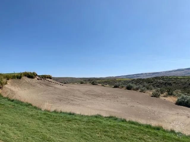A closer view of a flagstick at Gamble Sands, with a bunker beside the green and the mountains beyond.