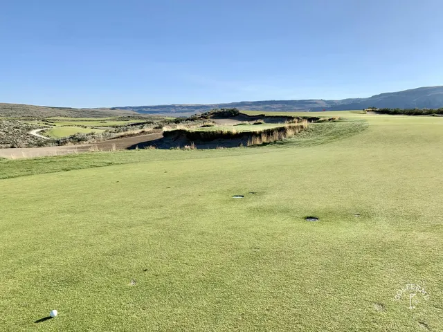 A tee shot at Gamble Sands with bunkers on both sides of the fairway and the mountains ahead.