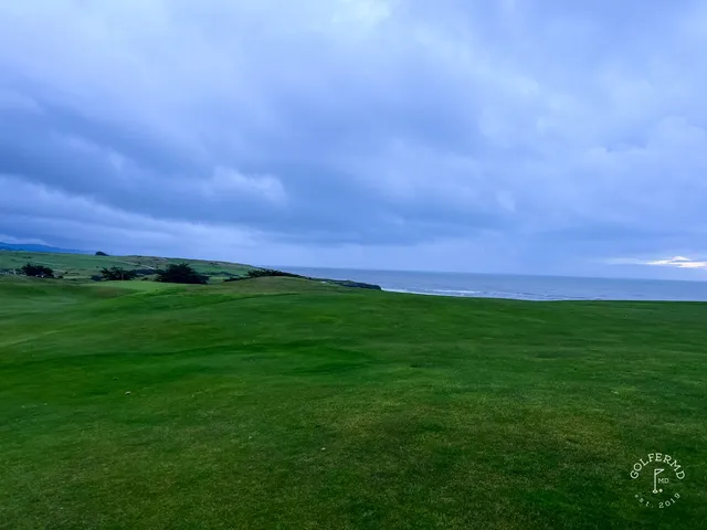 A green and flagstick on the bluff at Half Moon Bay Golf Links Ocean Course, with a bunker and the ocean beyond.