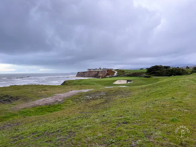 A green and flagstick above the ocean at Half Moon Bay Golf Links Ocean Course, with the Ritz-Carlton on the coast.