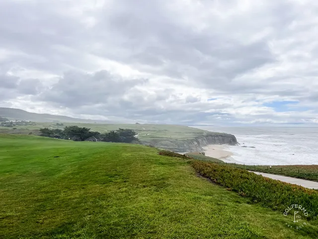 A green and flagstick above the ocean at Half Moon Bay Golf Links Ocean Course, with a wide bunker in front.