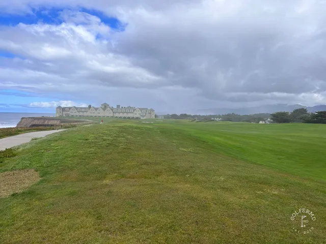 A green and flagstick above the ocean at Half Moon Bay Golf Links Ocean Course, with the coastline curving away.