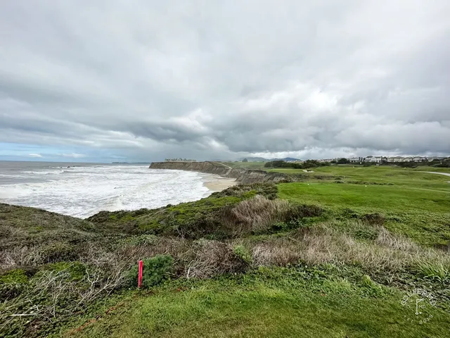 A golfer on a tee at Half Moon Bay Golf Links Ocean Course, with the ocean and the cliffs behind the hole.