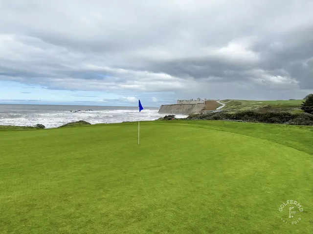 A golfer hitting a shot from a waste area at Half Moon Bay Golf Links Ocean Course, with the ocean behind the hole.