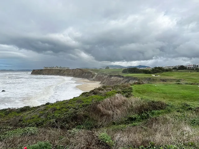 A green and flagstick above the ocean at Half Moon Bay Golf Links Ocean Course, with a bunker in front.