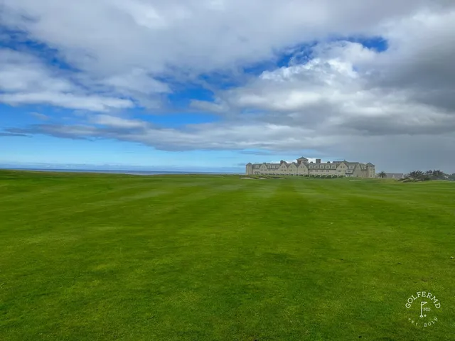 A green and flagstick above the ocean at Half Moon Bay Golf Links Ocean Course, with the coastline beyond.