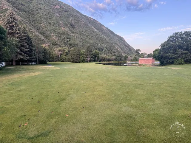 A green and flagstick at Hobble Creek, a bunker in front of the hole and the mountains beyond the trees.