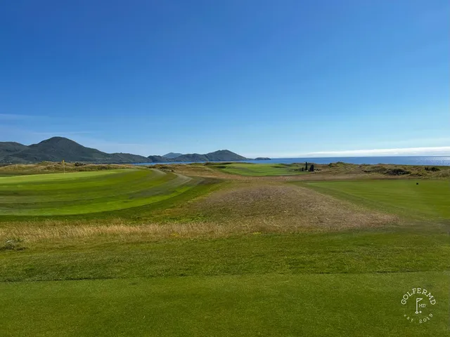 A close view of a green and flagstick at Hogs Head, with the water behind it.